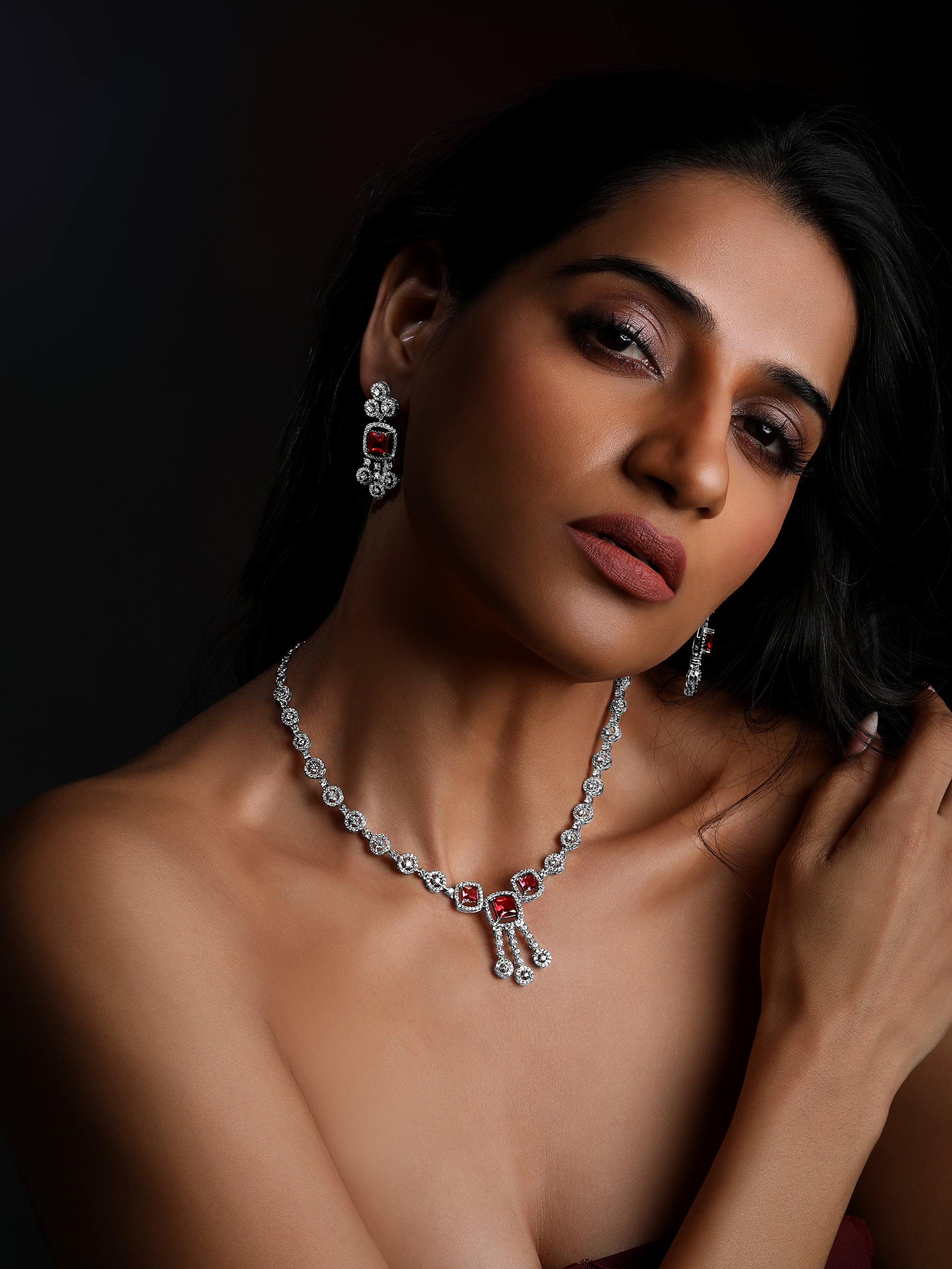Rhodium-plated red diamond necklace set with matching drop earrings studded with cubic zirconia on black stone background